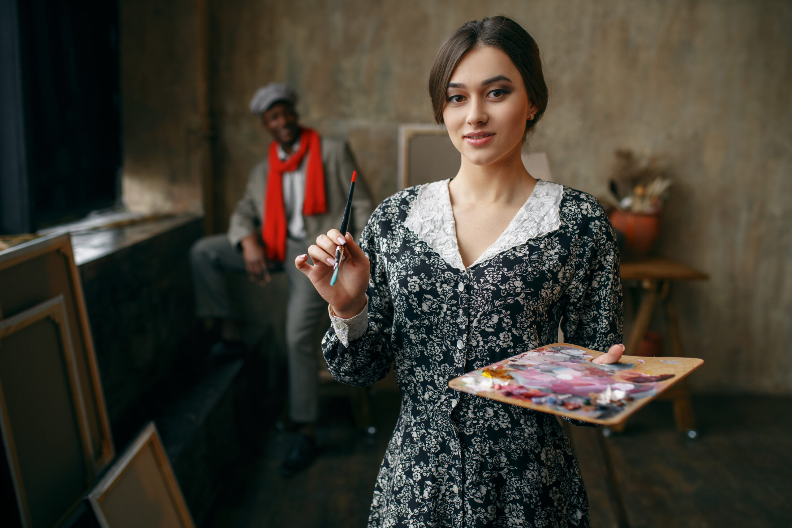 Female portrait painter holds palette and brush, male model in art studio on background. Male artist standing at his workplace, creative master in workshop